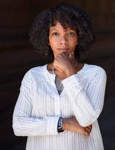 A portrait of a Black woman wearing a white shirt standing with her hand on her chin.